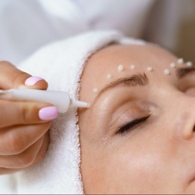 Cosmetologist applying cream on face